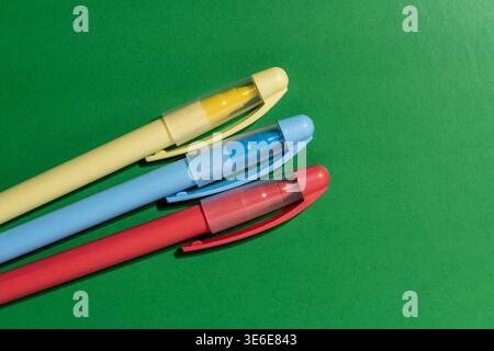 Close up of yellow blue and red plastic pens lying diagonally on bright green surface. Minimalist office stationery and back to school concept with co Stock Photo