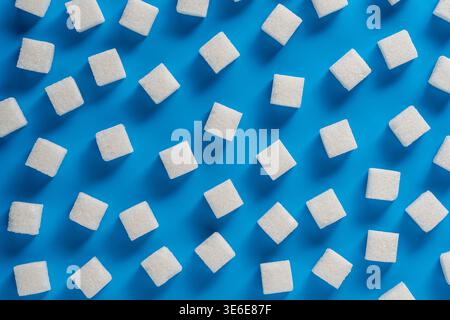 Top view of white refined sugar cubes scattered on a blue background. Creative flat lay food concept for health, nutrition, diabetes awareness, and cu Stock Photo