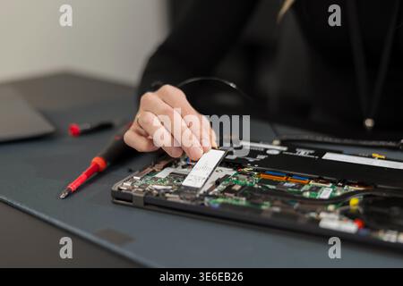 IT technician in his thirties repairs a laptop internals, upgrading components and diagnosing hardware issues Stock Photo