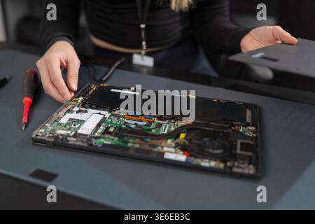 Female IT technician in her 20s repairs a laptop motherboard during a professional repair session Stock Photo
