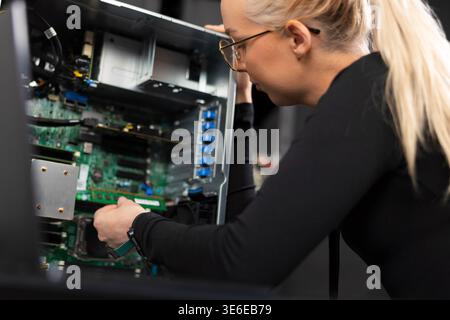Female IT technician upgrades and repairs server hardware in a data center, focused on diagnostics and maintenance Stock Photo