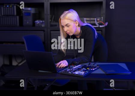 Female IT technician in her 20s repairing a laptop and motherboard in a tech lab Stock Photo
