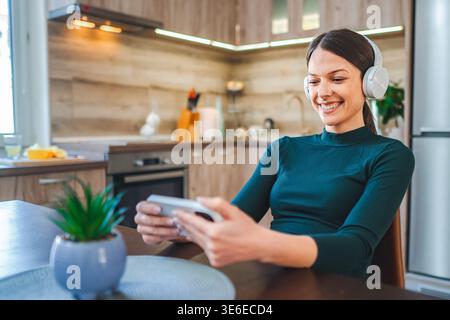 Young Woman Relaxing at Home, Watching Videos on Smartphone and Listening to Music with Headphones Stock Photo