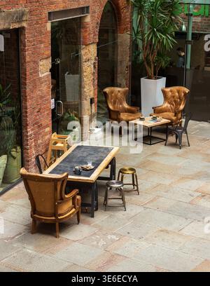 Leather armchairs and tables in the courtyard of the converted Royal Mill, Ancoats, Manchester, with red brick archway. Stock Photo