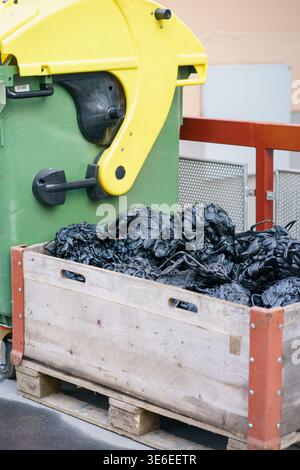 Pile of recycled rubber scrap in wooden crate near industrial processing machine, waste management, recycling industry, polymer material reuse concept Stock Photo