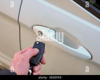 Hand pressing a car key remote button to unlock a white vehicle door handle, close-up of keyless entry technology and convenient, secure access to per Stock Photo