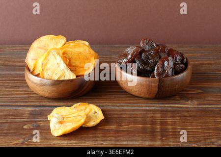 Dried apricots and persimmons in wooden bowls on a brown wooden table. Closeup Stock Photo