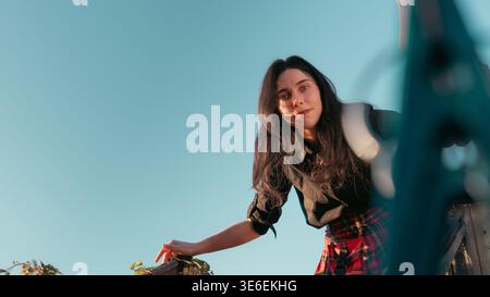 Outdoor portrait of a young woman standing against a clear blue sky in warm evening light. Creative low angle lifestyle image with relaxed pose, natur Stock Photo