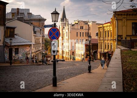 Scenic view of a historic city street with cobblestone road, elegant old buildings, street lamps, and pedestrians in warm evening light. Atmospheric u Stock Photo
