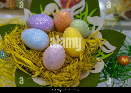 glittery pastel easter eggs nestled in yellow straw and green felt decorative leaves, creating a vibrant spring holiday centerpiece for festive celebr Stock Photo
