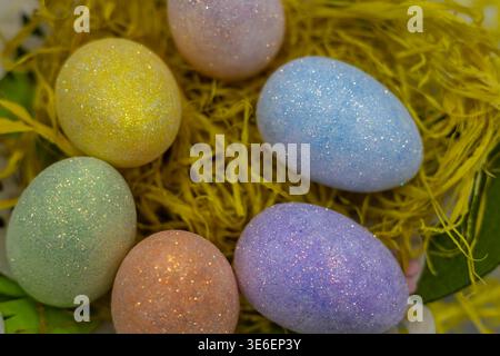 sparkling glitter-coated easter eggs in pastel colors nestled in a bed of yellow raffia. a festive and vibrant seasonal composition for spring holiday Stock Photo