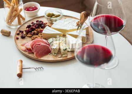 Elegant charcuterie board composition featuring assorted cheeses, cured meats, walnuts, dried cranberries, breadsticks, olives, and red jelly, paired Stock Photo