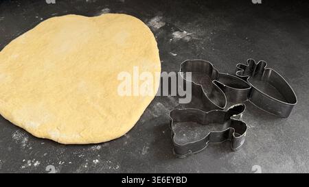 Rolled out dough on a dark countertop with various metal cookie cutters shaped like a bunny, carrot, and flower positioned nearby ready for baking Stock Photo