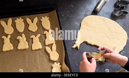 Baking Easter cookies with various shaped dough cutouts on a baking tray and a rolling pin on a home kitchen setting Stock Photo