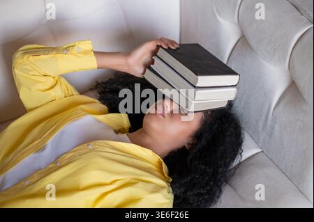 Brunette woman lying on the sofa and feeling tired after studying Stock Photo
