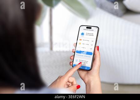 Person using medication reminder application on smartphone, managing pills and health routine in bright home environment with natural elements Stock Photo