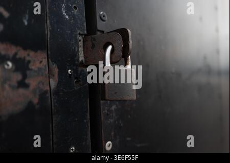 Durable steel lock on a weathered black door representing privacy and property protection in a commercial environment or storage facility for crime pr Stock Photo