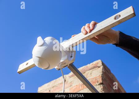 Hands checking the level of a white plastic CCTV camera mounted on a metal bracket. Security system, precise installation, technology setup. Stock Photo