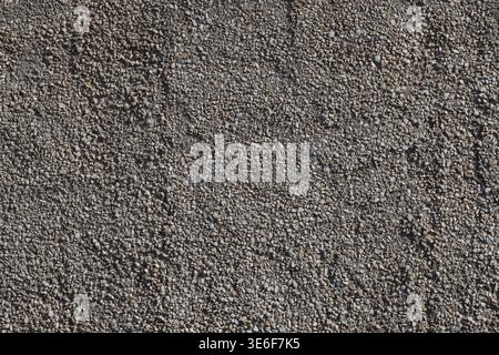 Close-up of rough plaster wall with small stones and marble chips, uneven surface, natural gray tones, outdoor facade texture. Stock Photo