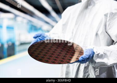 Holding processed silicon wafer, cleanroom and technician in automated fabrication plant. Engineer inspecting semiconductor substrate, defects and engineer doing quality control on microelectronics Stock Photo