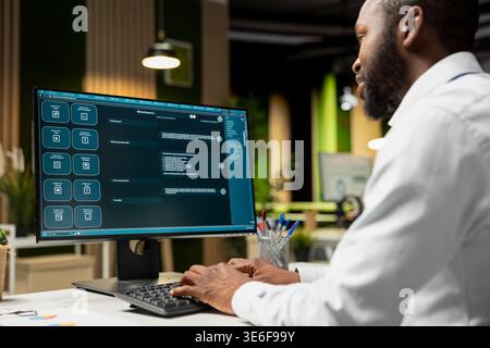 Black programmer developing an app and software algorithm on pc, working in the office late at night. Engineer uses digital tools and focuses on script engineering and coding, IT specialist. Stock Photo