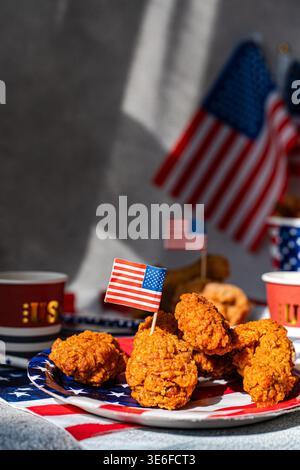 Crispy fried chicken wings served on a red, white and blue plate with small USA flags, festive table setting and cups, perfect for Independence Day pa Stock Photo