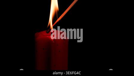 Candle flame burns brightly while a match ignites it in a dark setting during the evening Stock Photo