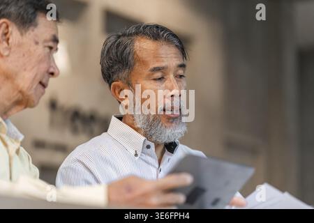 Two experienced businessmen engage in a strategic discussion at a cafe reviewing documents and using a tablet to share insights on an important projec Stock Photo