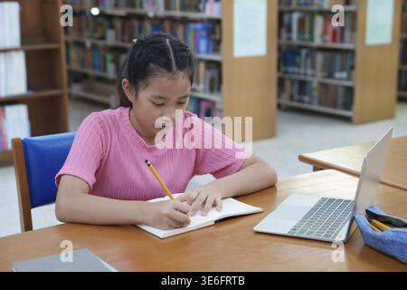 Online education, e-learning. Happy Asian elementary school girl in stylish casual clothes, studying remotely, using a laptop, listening to online lec Stock Photo