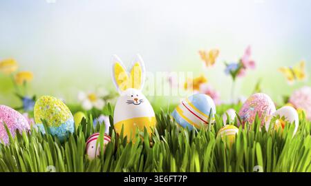 A bunny is standing in a field of Easter eggs. The eggs are scattered throughout the grass, with some being larger and others smaller. The bunny is th Stock Photo