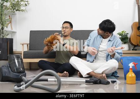 Two young men engage in a fun cleaning session, using household items as musical instruments. Concept of friendship and joy in chores Stock Photo