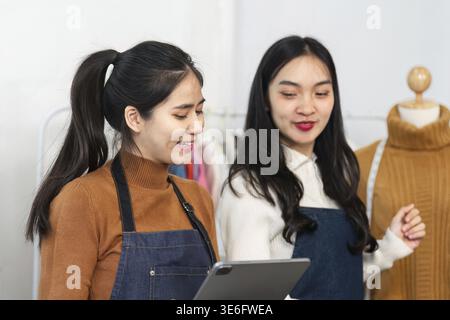 Two female fashion designers working together in a boutique, discussing ideas and designs while displaying their tailored clothing collection Stock Photo