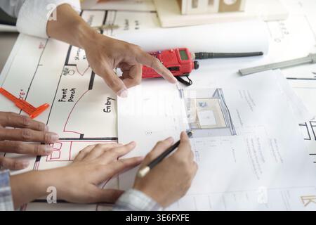 Two engineers pointing at detailed architectural plans, collaborating on design and project execution in a bright office Stock Photo