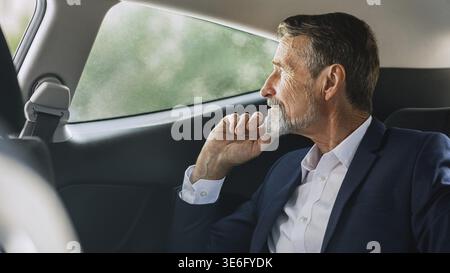Side view of mature businessman sitting on a backseat of a car and looking out of window Stock Photo