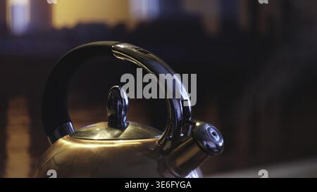 Polished kettle boiling on a gas stove in the kitchen in the evening. Close up of boiling kettle with the steam coming from metal teapot on gas oven Stock Photo