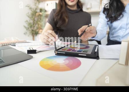 Two women architects collaborating on color choices and design elements using a tablet in a modern office setting Stock Photo