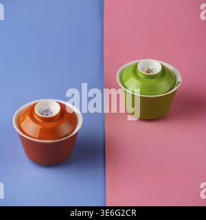 Two stylish ceramic bowls in orange and green on a pink and blue backdrop, perfect for vibrant decor Stock Photo