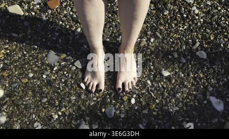Top view of feet at the beach with sea waves. Connecting to nature, beautiful legs and feet of a woman with her nails painted black being washed by se Stock Photo