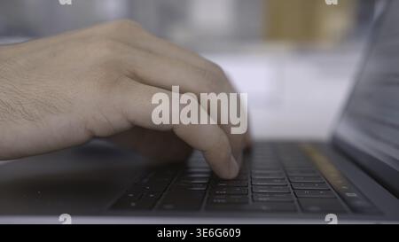 Side view of hands pressing keys of black laptop keypad. Close up of a keayboard and man hands typing on modern computer on blurred background Stock Photo