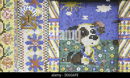 Unusual facade an old wooden house decorated by colorful mosaic pictures from small plastic bottle caps, creativity concept. Beautiful and bright hand Stock Photo