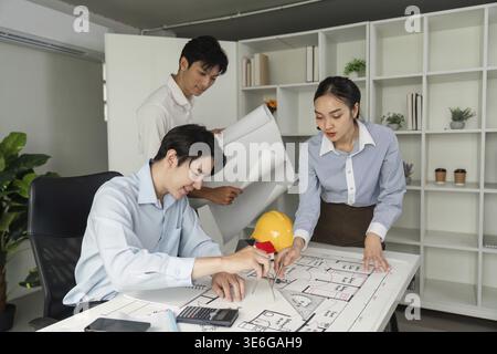 Three architects gather around a table with architectural plans, collaborating on a project while sharing ideas and strategies for successful executio Stock Photo