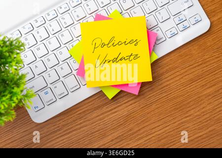 A yellow sticky note with Policies Update handwritten text on a white computer keyboard. Corporate policy changes, office administration Stock Photo