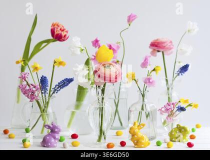 Beautiful flowers bouquets in glass vases on festive Easter table. Colored Easter eggs in egg cups Stock Photo