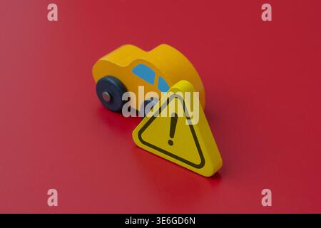 A toy car and a warning triangle on a red background. Road safety, car accidents, vehicle insurance, hazard warning concept. Stock Photo