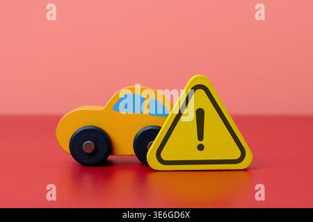 A toy car and a warning triangle on a red background. Road safety, car accidents, vehicle insurance, hazard warning concept. Stock Photo