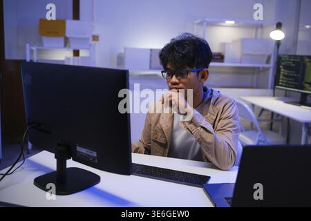 Male Software Engineer Writing Code on Desktop Computer with Multiple Screens Setup. Data center programmer managing large datasets used in AI trainin Stock Photo