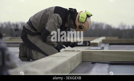 Side view of a man worker in uniform and protective helmet setting laser level tool at the construction site. Male builder using laser spirit level to Stock Photo