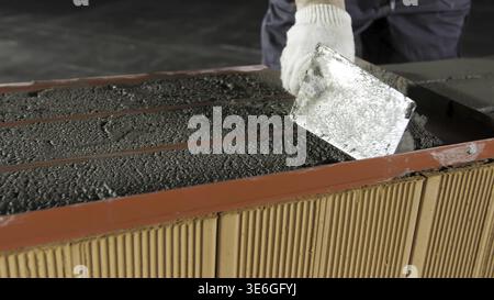 Construction worker using trowel for levelling raw mortar for the brick layers fixation. Close up of cement being put on red bricks Stock Photo