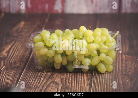 Green grapes in a plastic container on wooden table Stock Photo