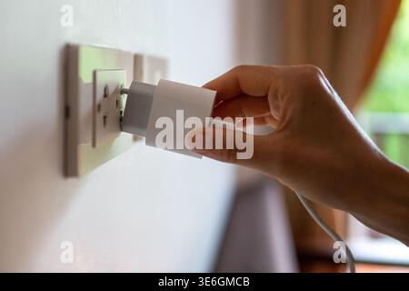 Woman hand holding mobile charger plugging in outlet on wall in room, problematic charging in hotels Stock Photo
